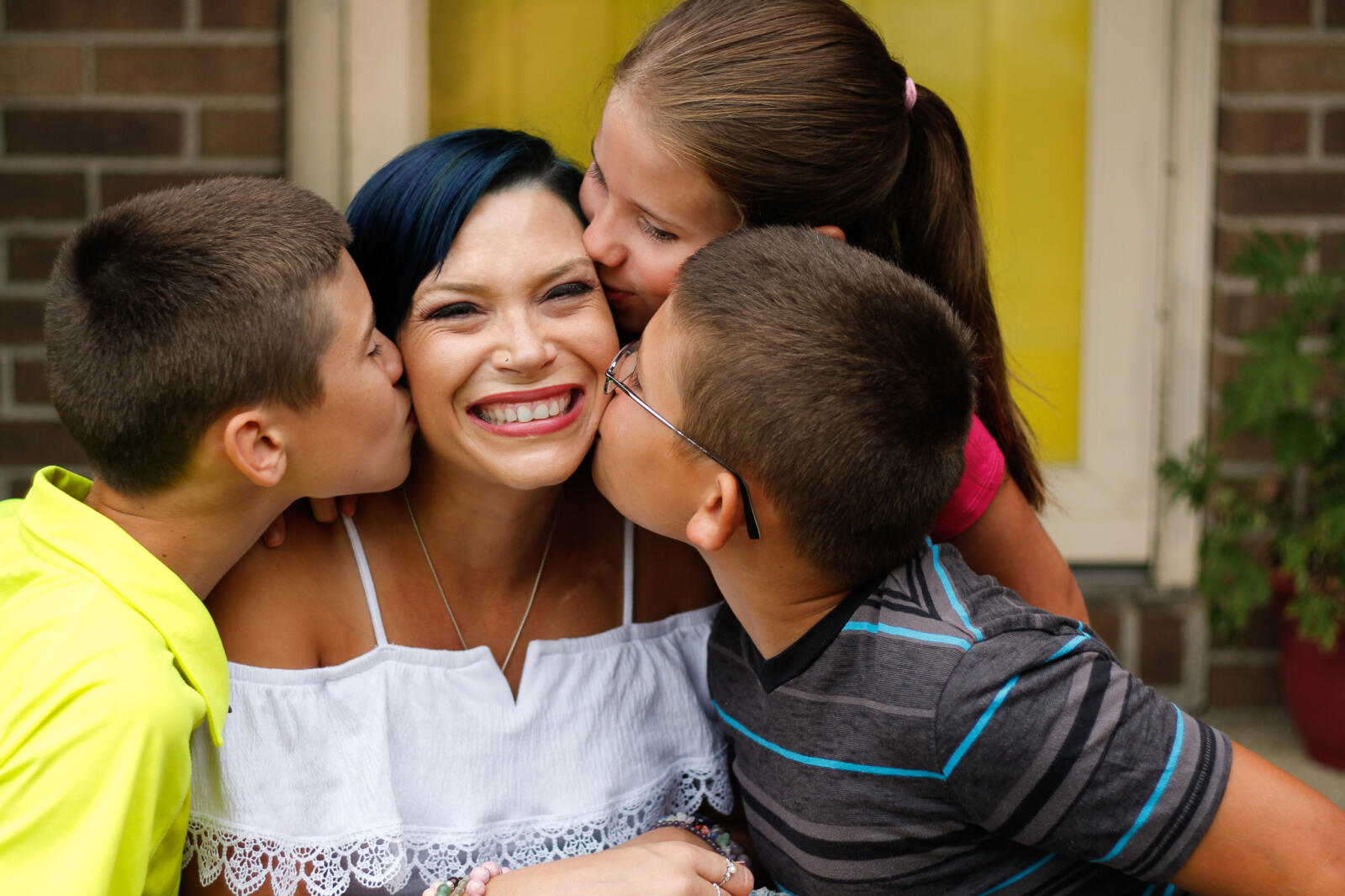 Mom is kissed by her three happy children. She has huge smile on her face.