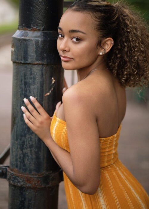 lack Model with curly Hair and a mustard yellow striped dress standing.
