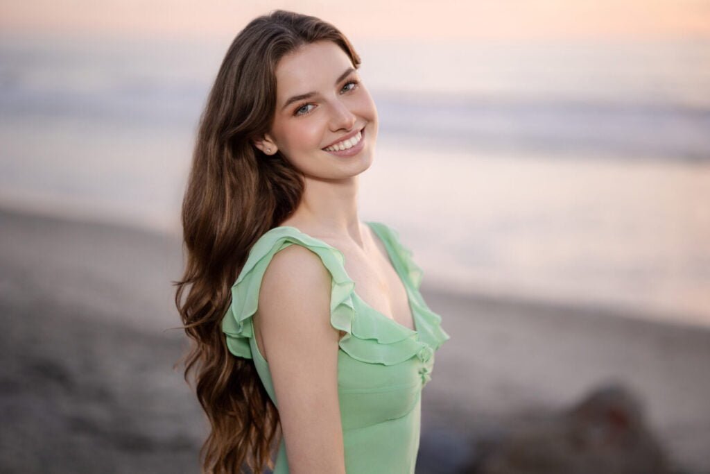 High School Senior with beach and ocean behind her. Wearing a soft green dress and long curled hair.