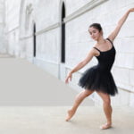 Gallery image of Dancer in Black dress with white bricks behind her.