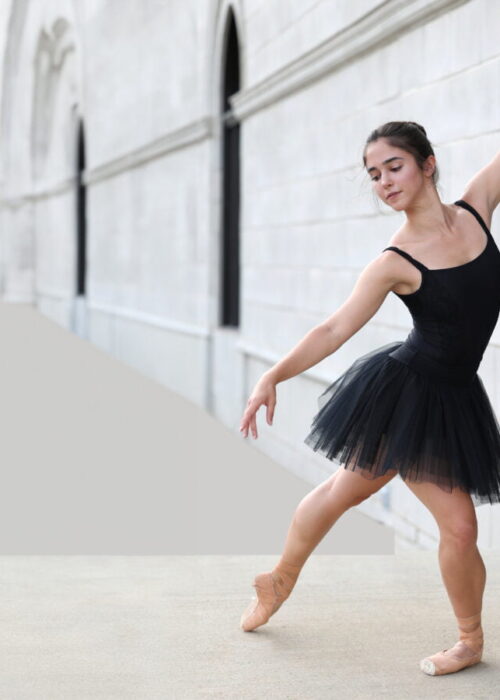 Dancer in Black dress with white bricks behind her.